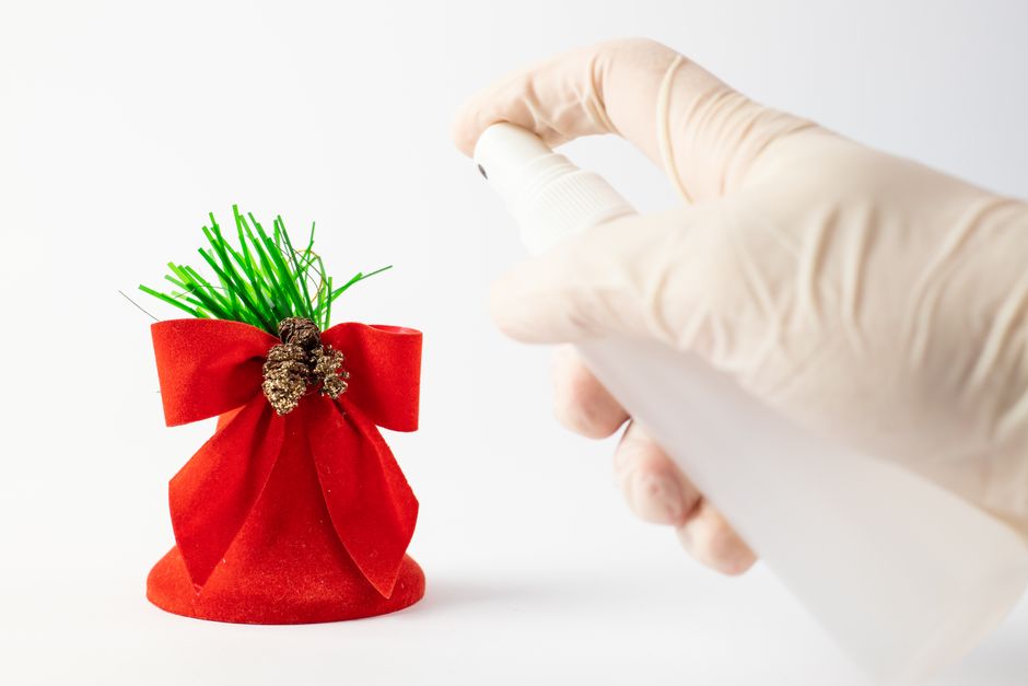 Close-up of a gloved hand spraying a red holiday decoration with a bottle.
